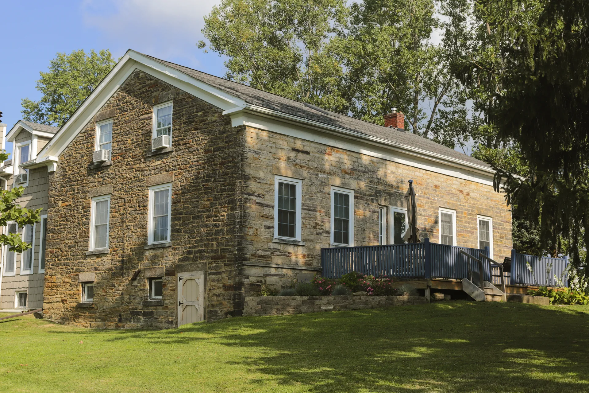 The weathered stone flank of the house with its blue porch deck