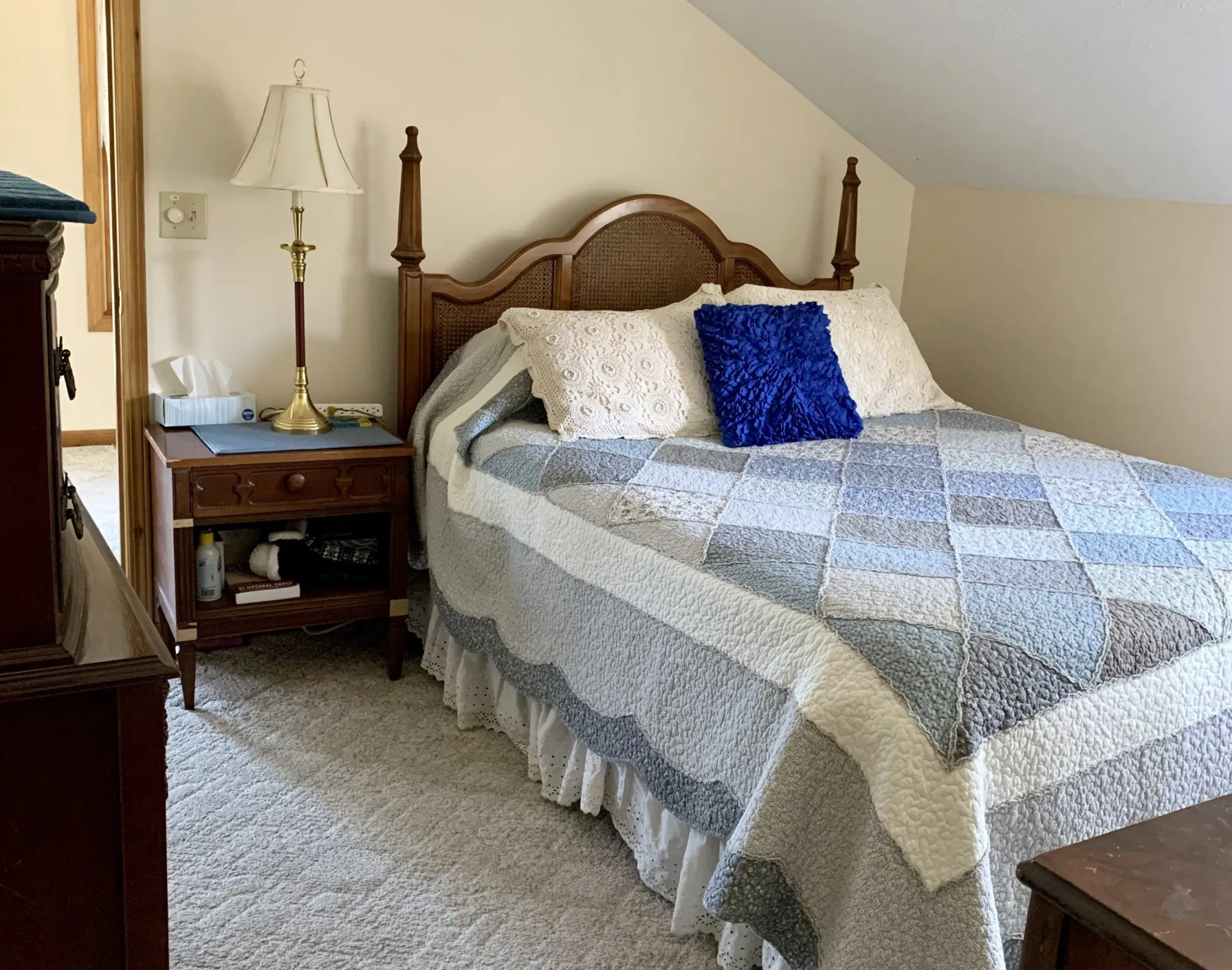 A quiet upstairs bedroom with a quilted bed beneath a sloped ceiling