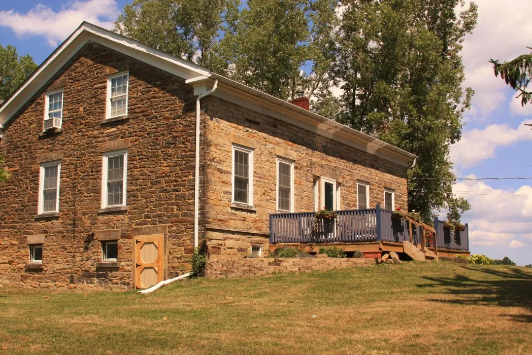 The south face of the Old Stone House with its blue porch deck and stone showing purple and blue mineral bands